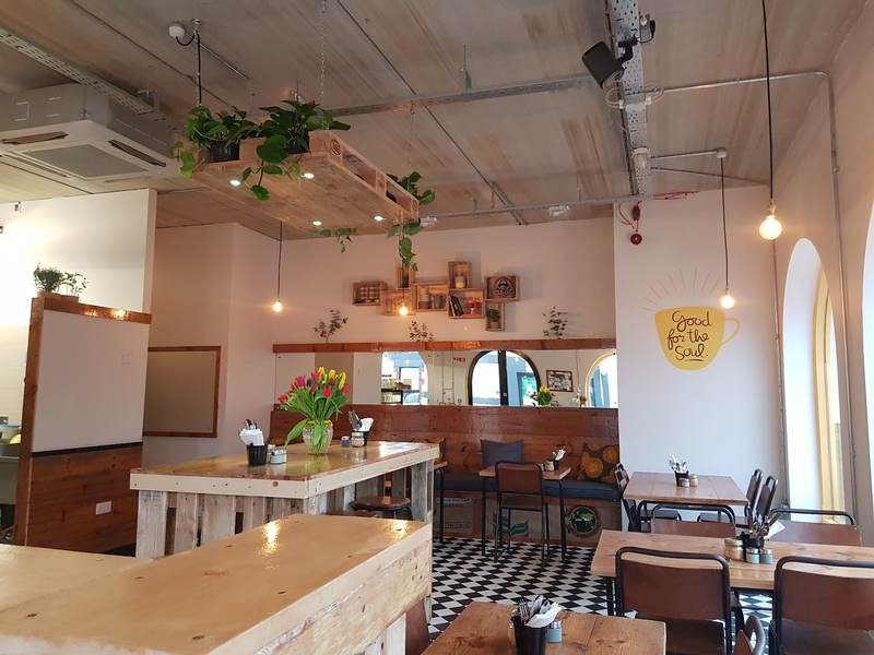 Inside the café: hanging plants, wooden tables, a black and white tiled floor and the yellow cup logo on the wall