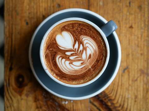 A latte with leaf art on a wooden table