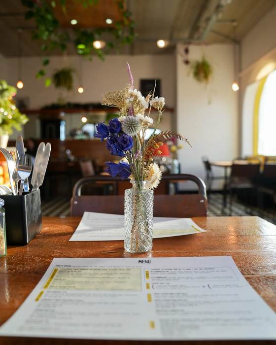 A table with a small vase of flowers and a printed menu, the café behind